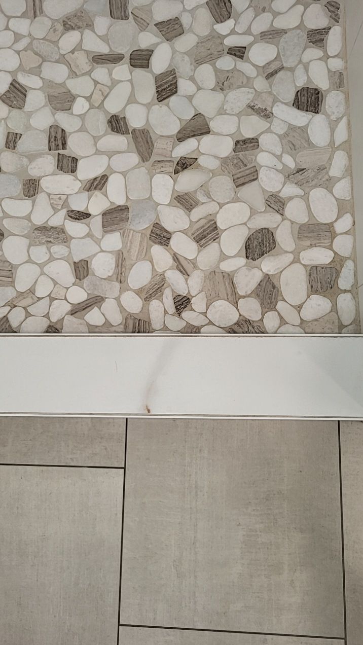 Pebble mosaic shower floor meeting large-format tile